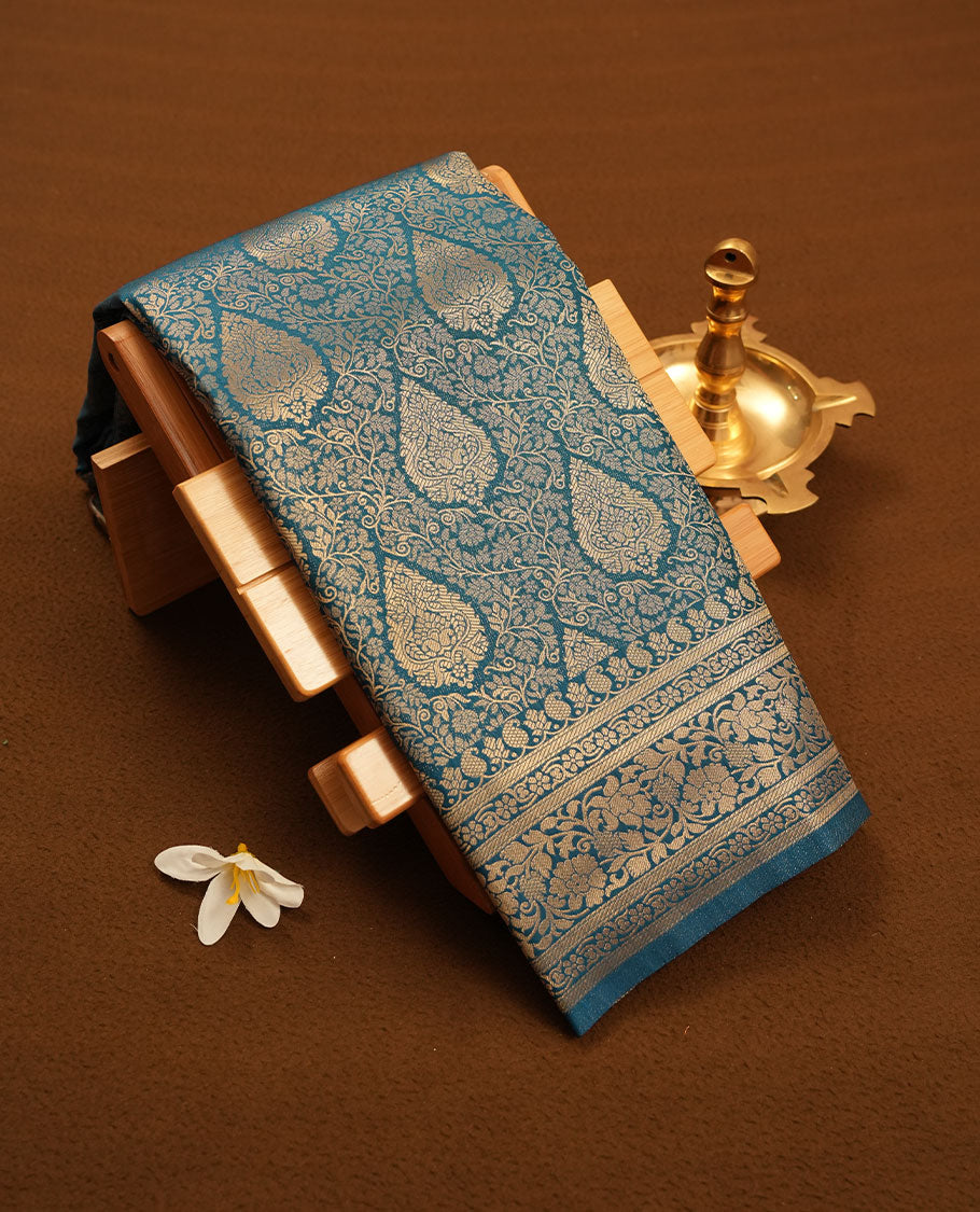 Teal blue colour semi silk brocade saree featuring intricate Gold Floral kodi patterns across the body, complemented by a Self colour woven border and pallu, paired with a matching blouse.