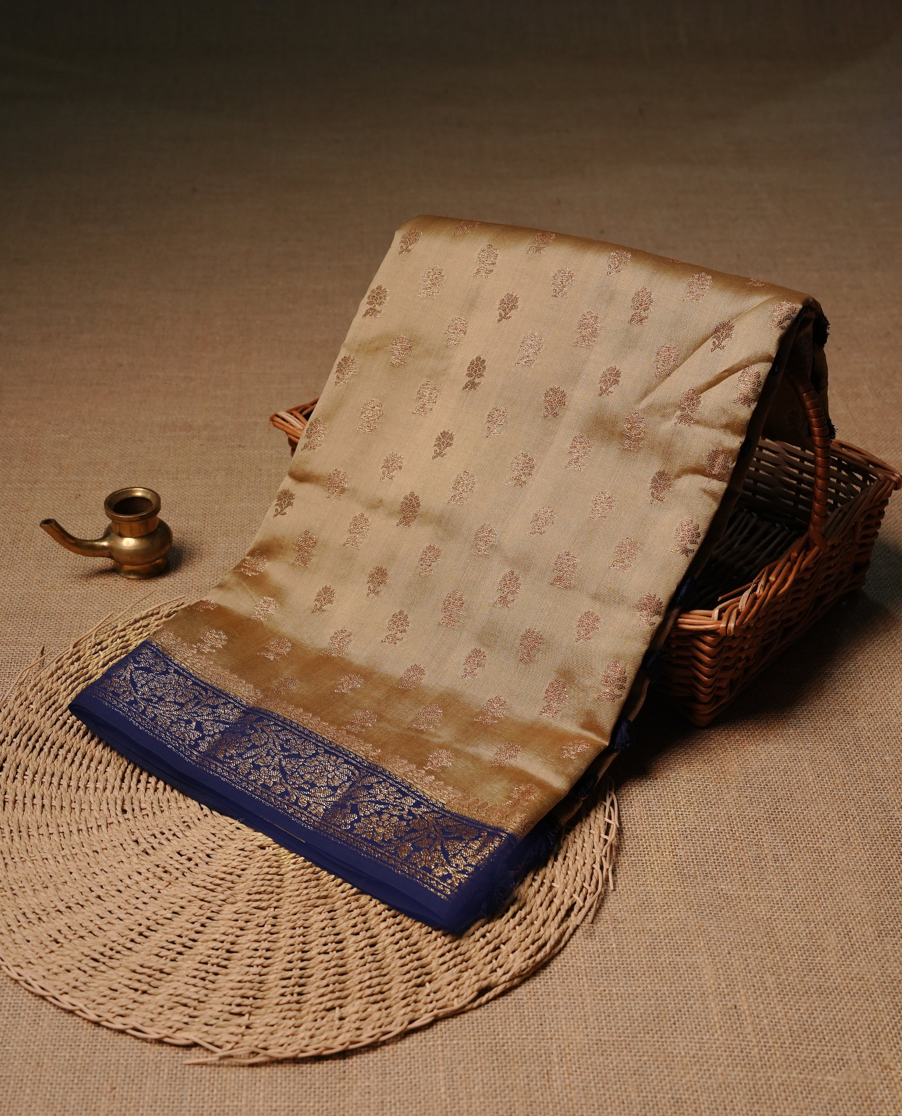 Cream colour Banaras tussar silk saree featuring elegant gold zari buttas across the body, complemented by a contrast Navy Blue border with rich zari detailing. Comes paired with a matching blouse piece.