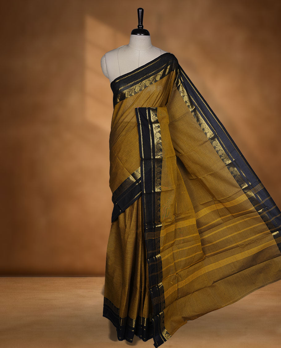 Dark mustard yellow colour chettinad cotton saree featuring plain body, paired with a black colour traditional gold zari border without blouse.