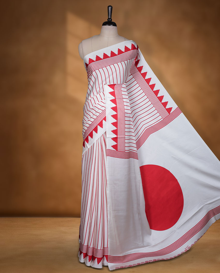 White colour semi modal saree highlighted with bold red triangle borders and fine striped detailing across the drape, featuring a striking oversized red circular motif on the pallu, paired with an all-over printed matching blouse.