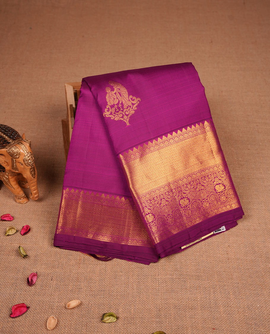 Rich magenta colour pure traditional Kancheepuram silk saree adorned with an elegant zari motif on the body, complemented by a grand gold zari woven border with intricate traditional patterns, paired with a matching blouse piece.