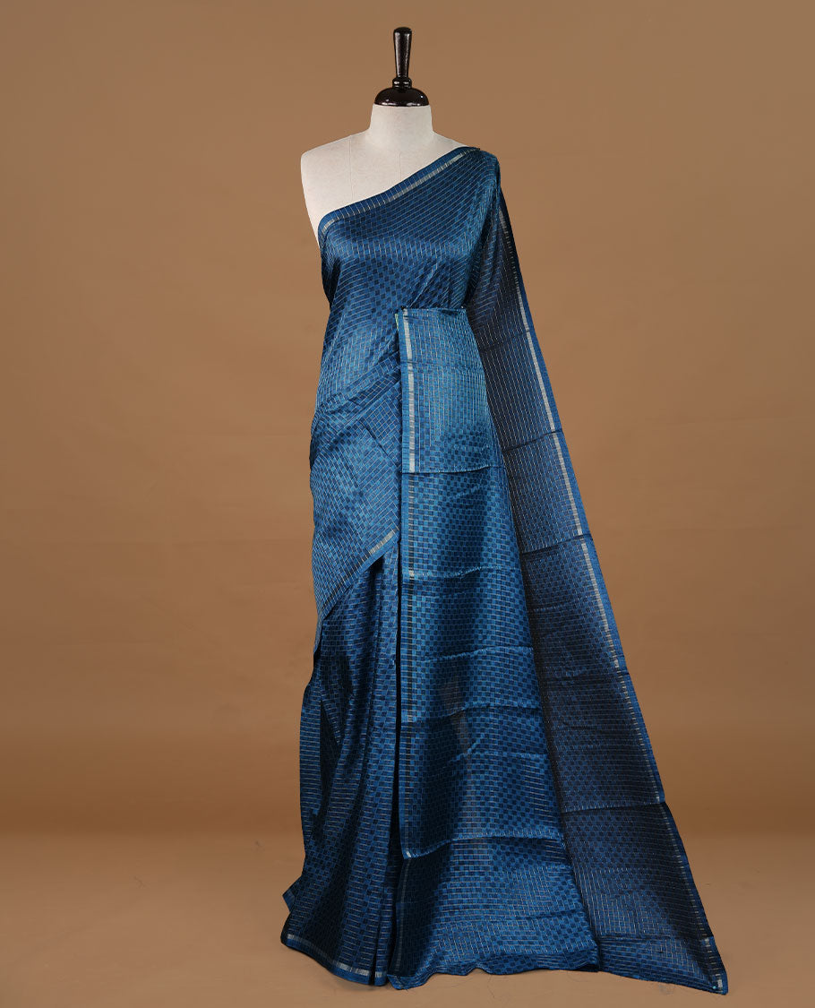 Peacock blue colour Semi Tussar saree featuring an elegant zari fancy check pattern on the body, highlighted with a small border for a refined look. Comes without a blouse piece.