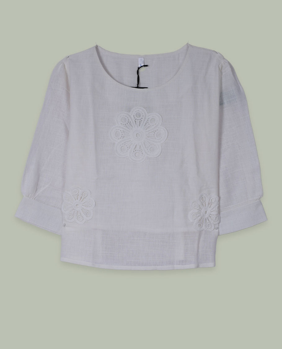 White three-quarter sleeve top with round neckline and tonal crochet floral appliqués placed at the center front and near the hem.
