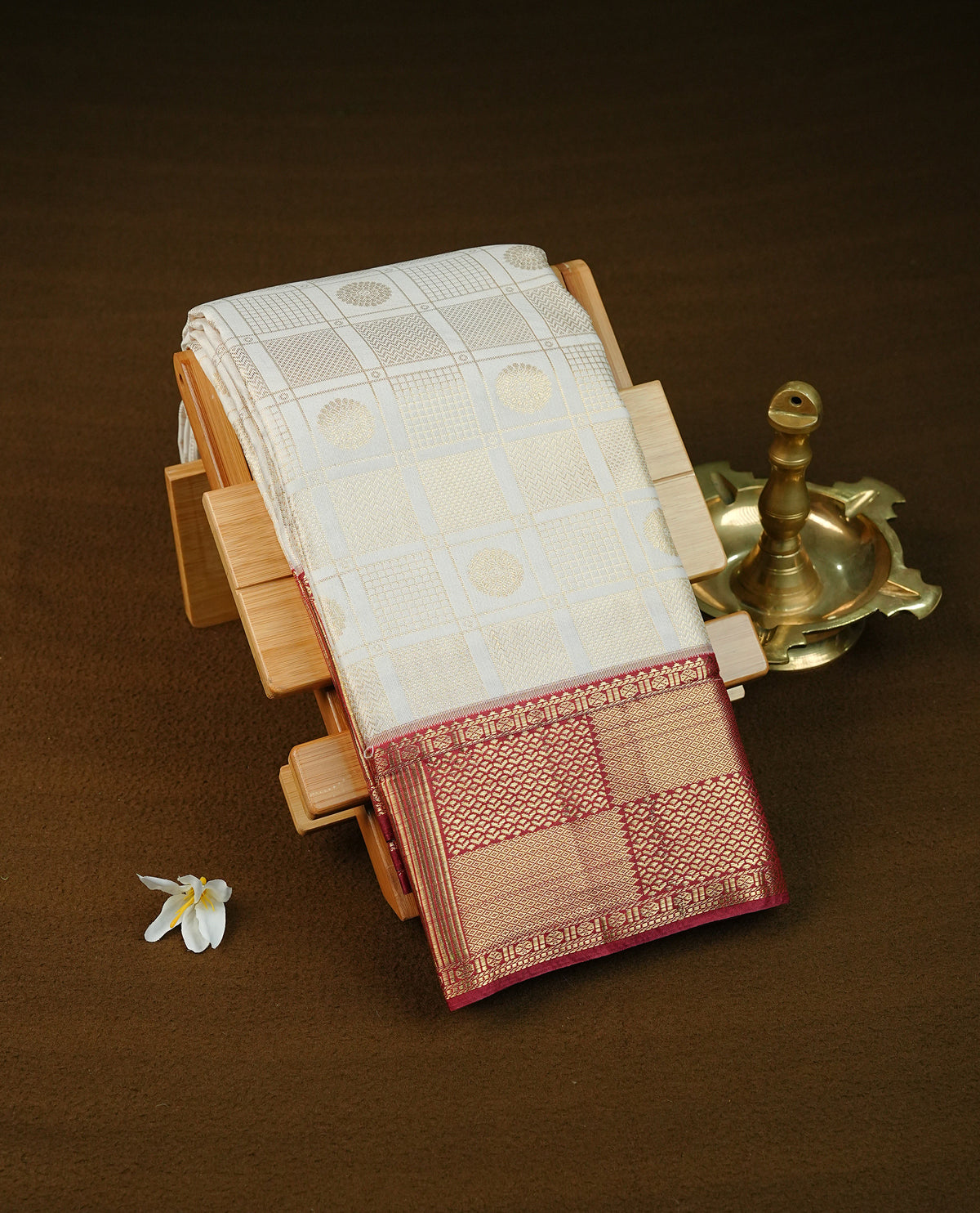 Cream colour semi wedding saree featuring light gold zari box with check with chakra across the body, complemented by maroon colour with traditional border. Comes with a matching blouse piece.