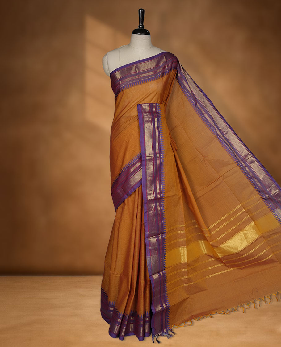 Brown colour chettinad cotton saree featuring elegant plain body highlighting contrast indigo colour with gold zari traditional border, pallu and paired with matching blouse piece.