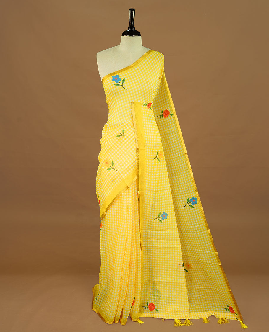 Yellow colour Semi Linen saree featuring a stylish check pattern adorned with floral prints on the body, enhanced by a small gold border, paired with a matching blouse piece.