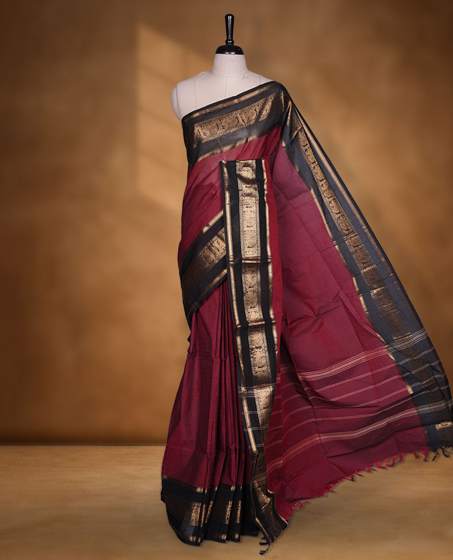 Dark red colour chettinad cotton saree featuring plain body, paired with a black colour traditional gold zari border paired with matching blouse.