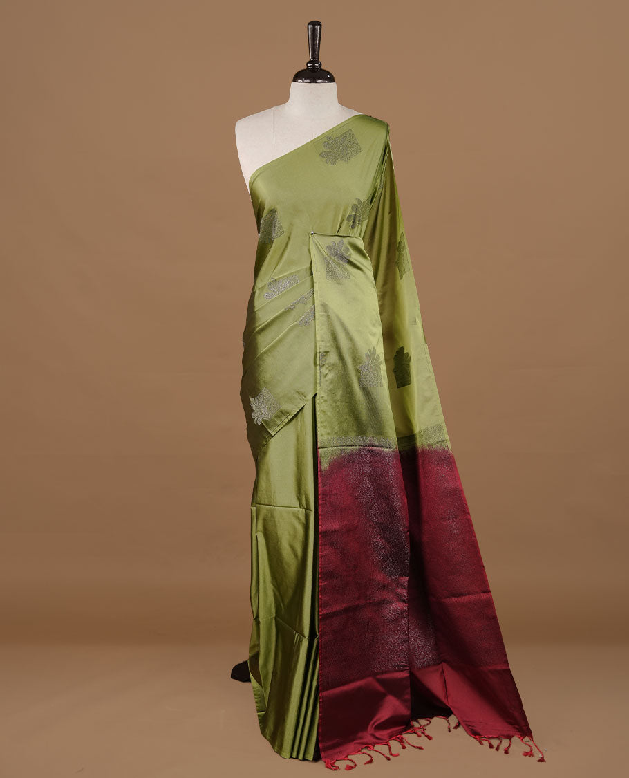 Olive colour soft silk saree features a sleek borderless design with intricate antique zari motifs, flowing into a striking contrast red pallu and a matching blouse piece.