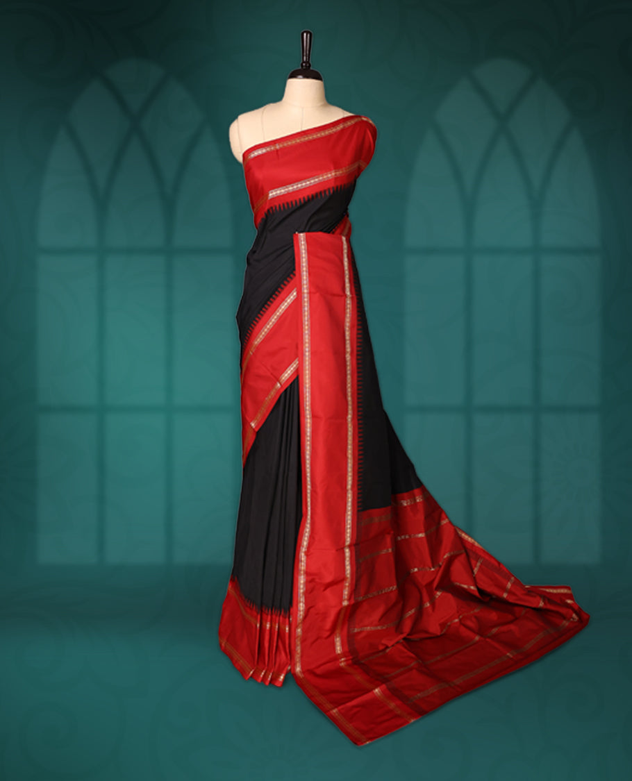 Black semi silk saree with plain body, vibrant red pallu and rich red border adorned with golden zari, accented with temple motifs along the edges, Paired with a matching blouse, perfect for festive occasions.