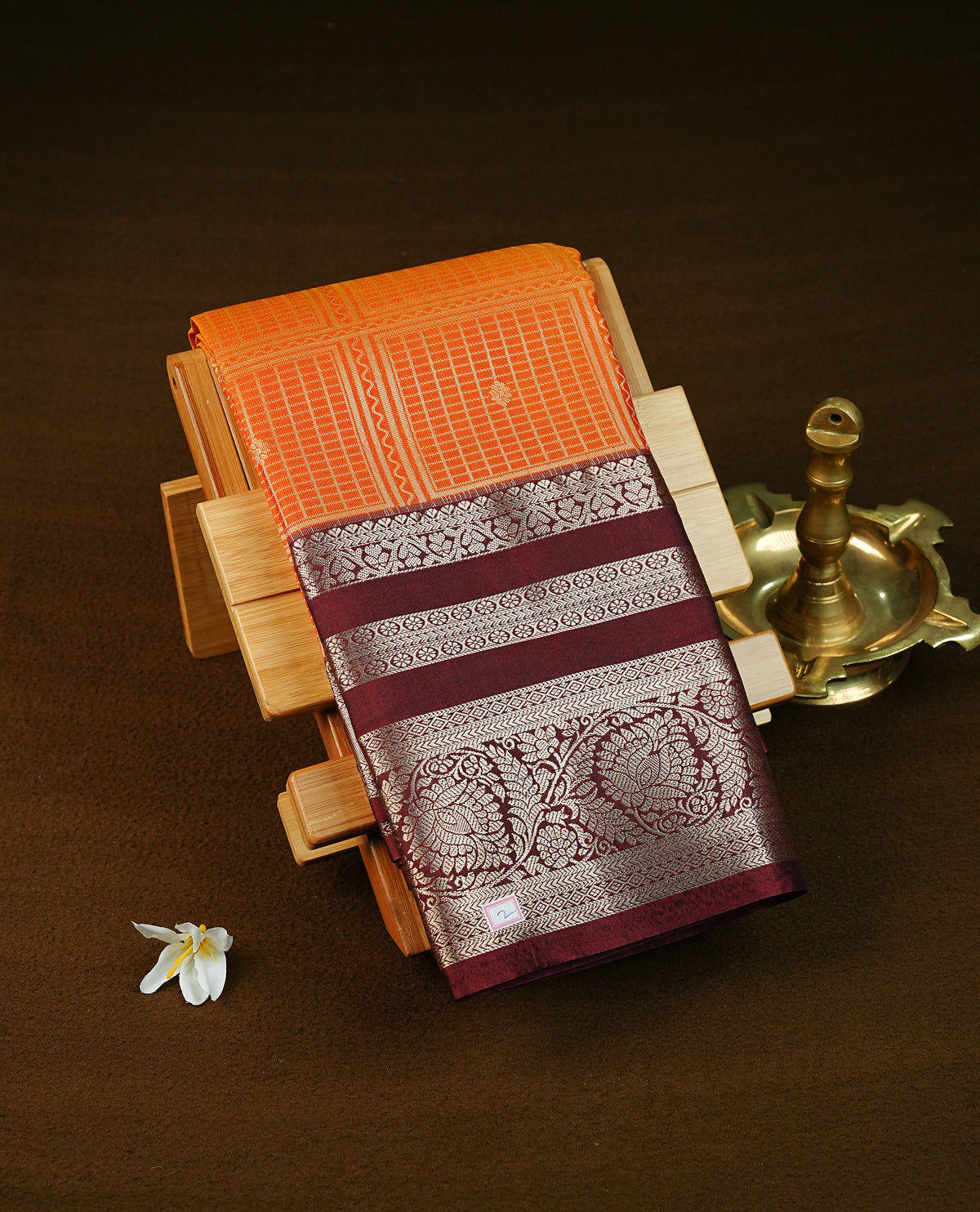 Rust orange colour semi wedding saree featuring gold zari box with check pattern with motifs across the body, complemented by contrast brown colour traditional border. Comes with a matching blouse piece.