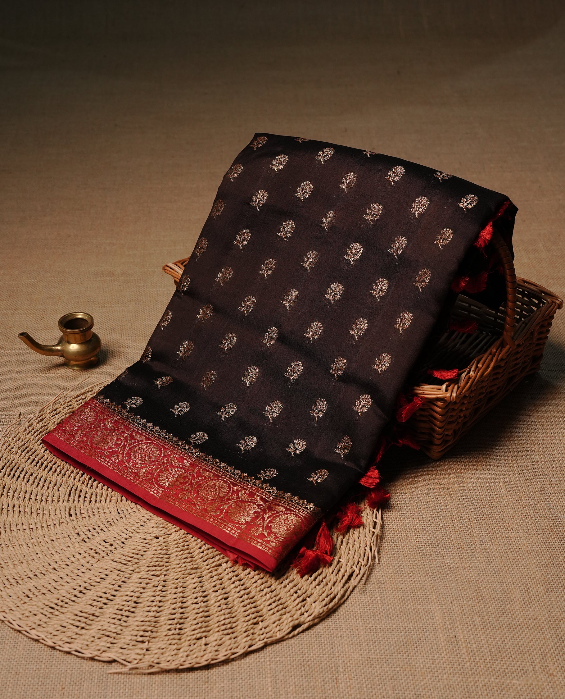 Chocolate colour Banaras tussar silk saree featuring elegant gold zari buttas across the body, complemented by a contrast Red border with rich zari detailing. Comes paired with a matching blouse piece.