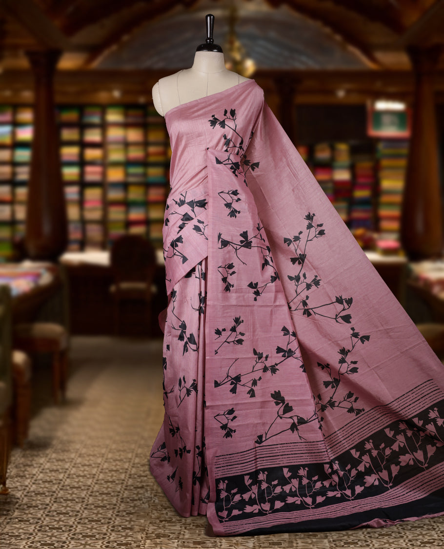 Pastel Pink colour Semi tussar silk saree adorned with black floral prints on the body and an elegant pallu & Comes with a matching blouse piece for a classy look.