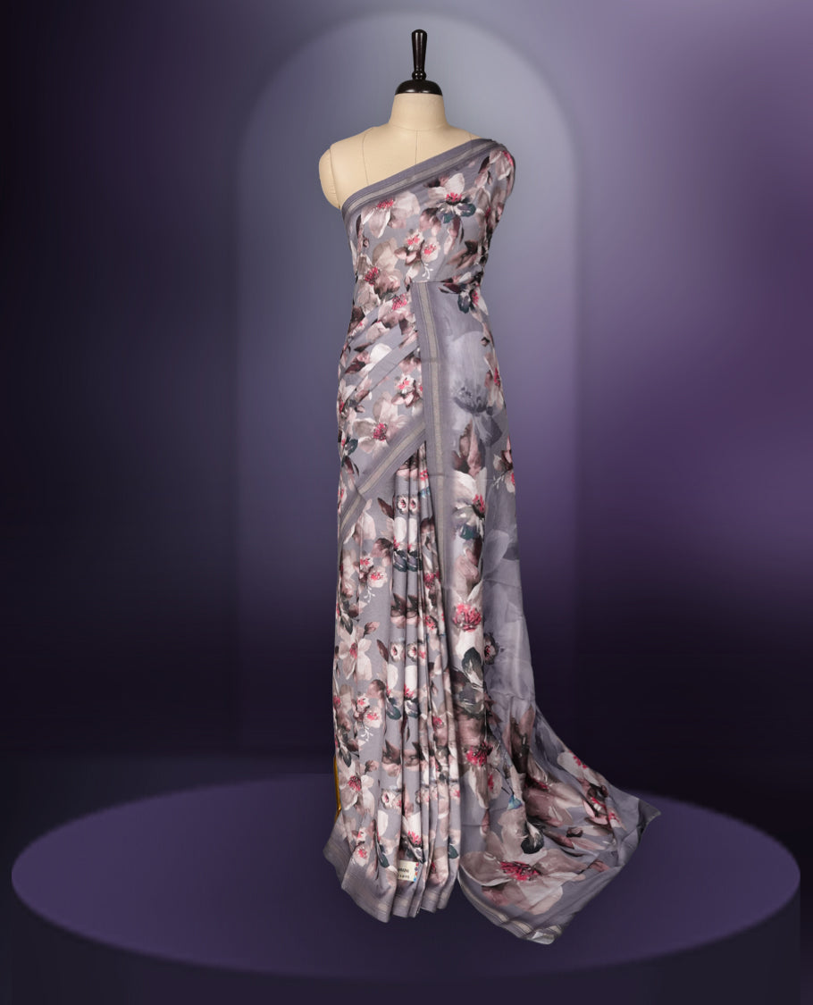 Grey colour saree adorned with elegant floral prints on the body, enhanced with a subtle matching border, complemented by a beautifully printed pallu featuring blooming flowers, and paired with a matching blouse.