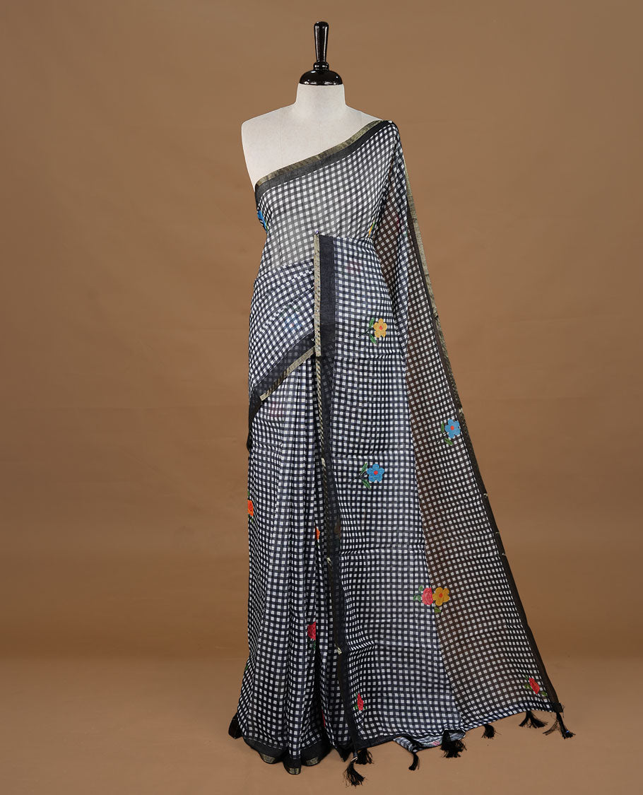 Black colour Semi Linen saree featuring a stylish check pattern adorned with floral prints on the body, enhanced by a small gold border, paired with a matching blouse piece.