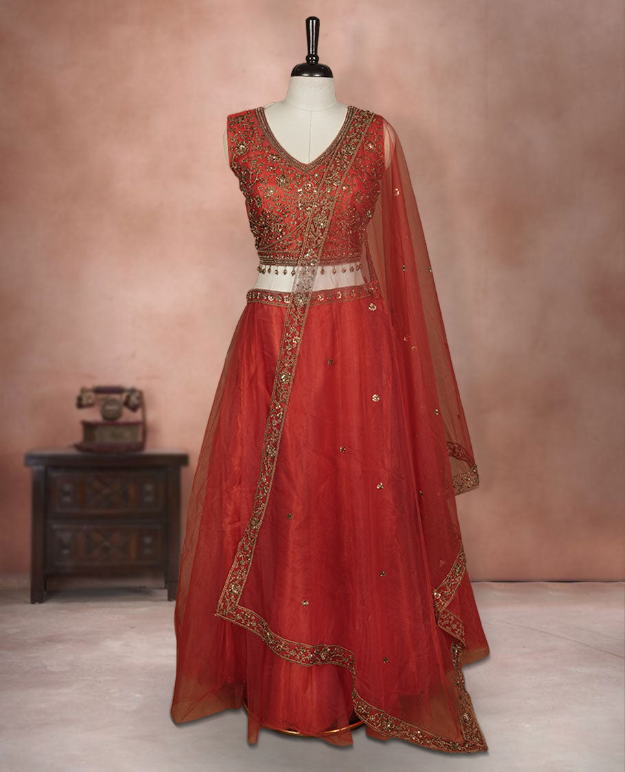 Red colour lehenga set with stitched sleeveless Antique thread embroidered & beats worked blouse featuring sheer neckline, matching stitched flared lehenga, and plain sheer dupatta.