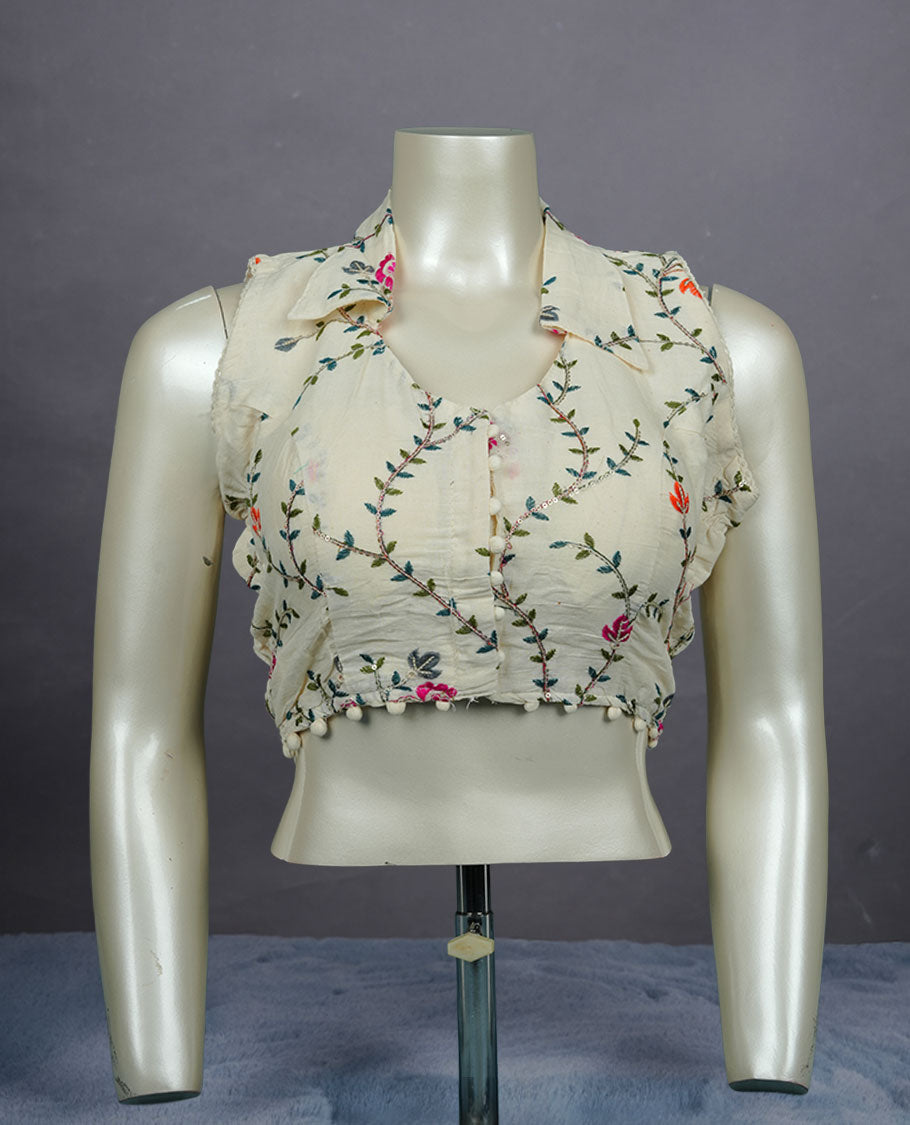 Cream colour sleeveless embroidered blouse with soft collar, front button detailing, delicate vine motifs, and pom-pom hem finish.