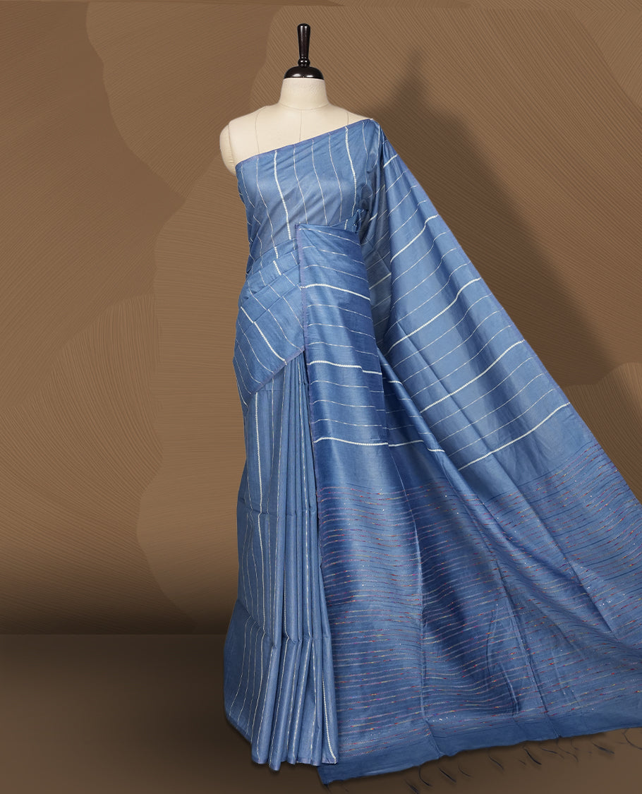 Blue colour semi jute saree with vertical white stripes for a modern appeal, Soft texture, sleek border, tassel pallu, and subtle multicolor detailing & Includes matching blouse piece for a complete look.