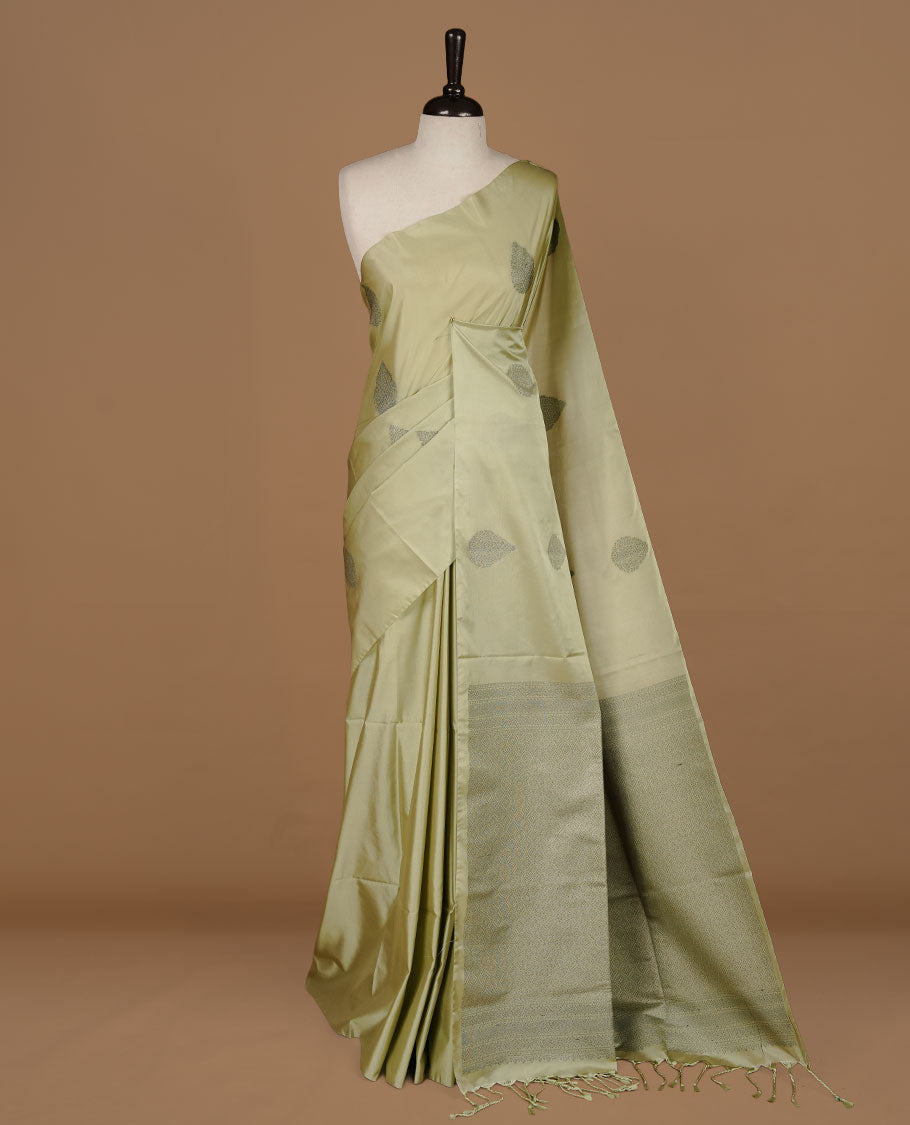 Tea green soft silk saree features a sleek borderless design with intricate antique zari motifs, flowing into a seamless self colored pallu and a matching blouse piece.