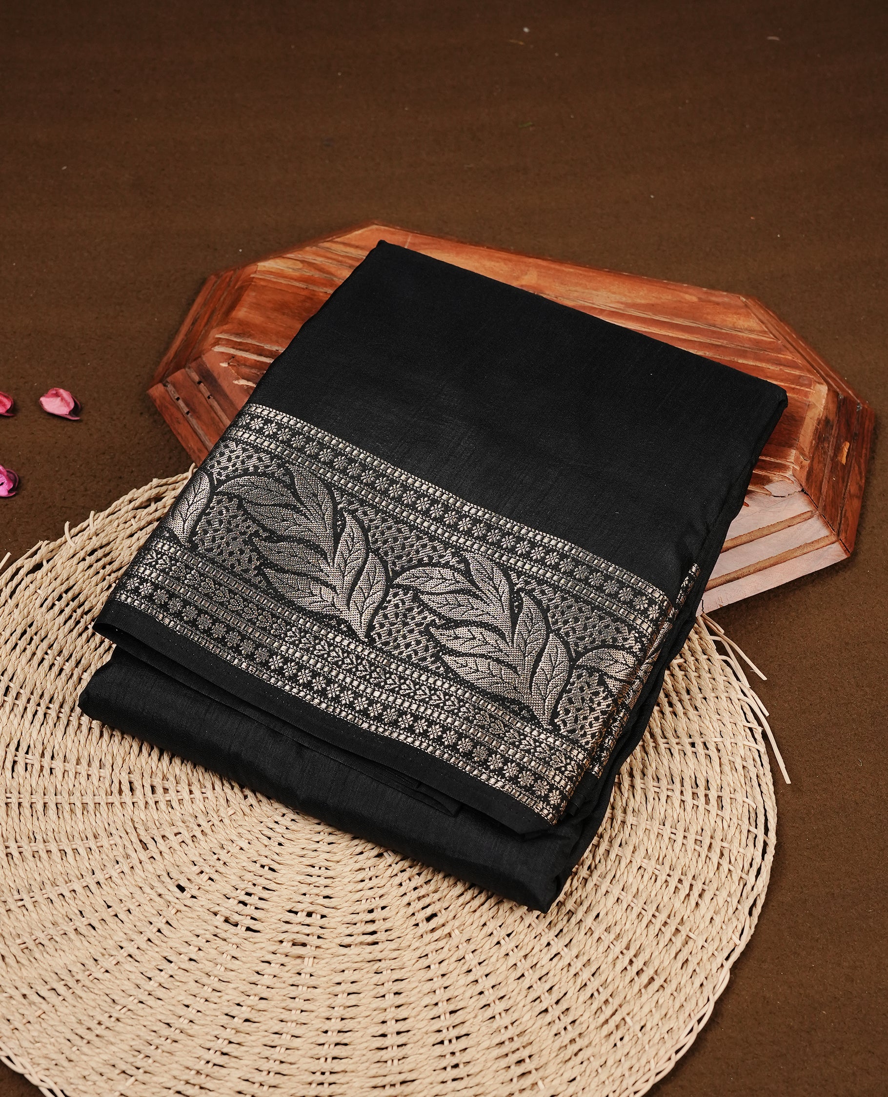 Black colour semi Tussar silk saree featuring an elegant plain body, complemented by a self colour border adorned with traditional gold zari floral kodi patterns. Comes paired with a matching blouse piece.