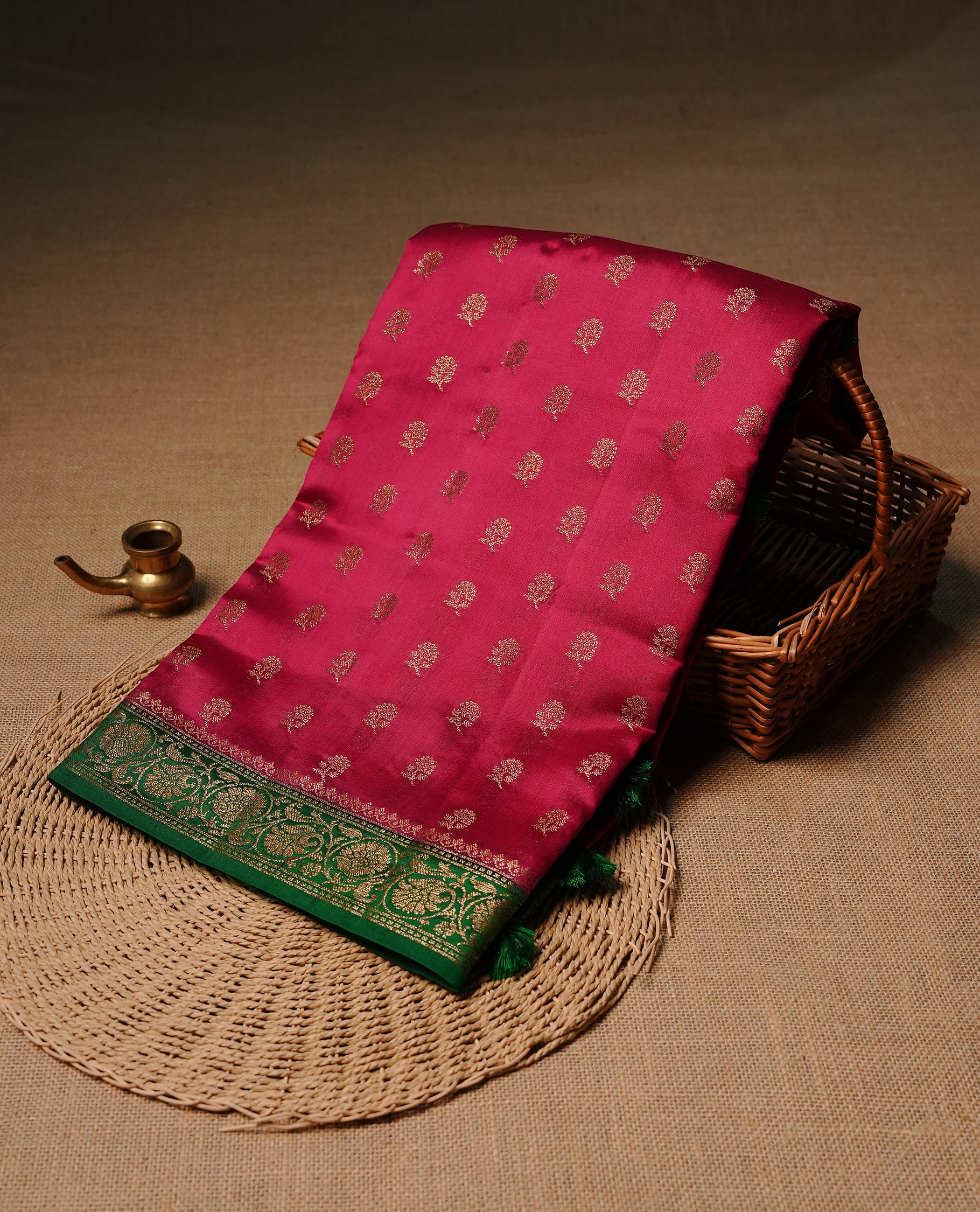 Magenta colour pure tussar Banaras silk saree featuring intricate gold zari motifs across the body, enhanced with a contrast green floral kodi zari border for a rich traditional look. Comes with a matching blouse piece.