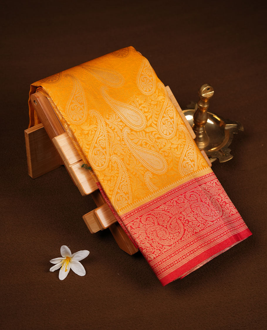 Mustard yellow colour semi soft silk brocade saree featuring elegant gold woven motifs across the body, highlighted with a contrasting red richly detailed border and pallu, paired with a matching blouse piece.