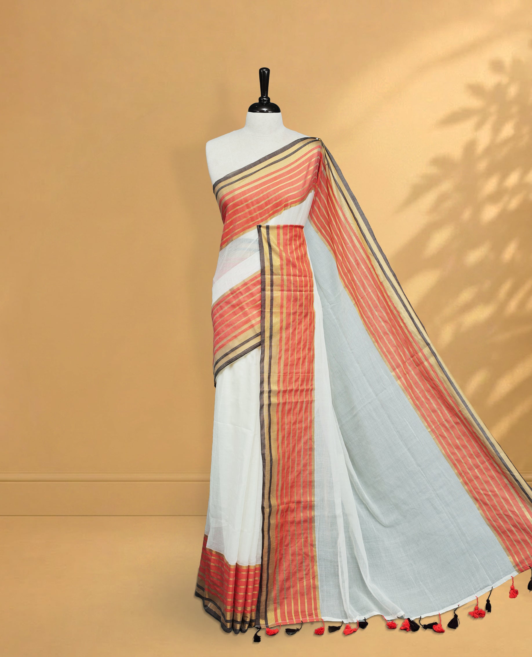 Off White Colour Mul Cotton Saree featuring Elegant Plain Body, Contrast Gold, Orange & black Border and Tassels Onam inspired charm.