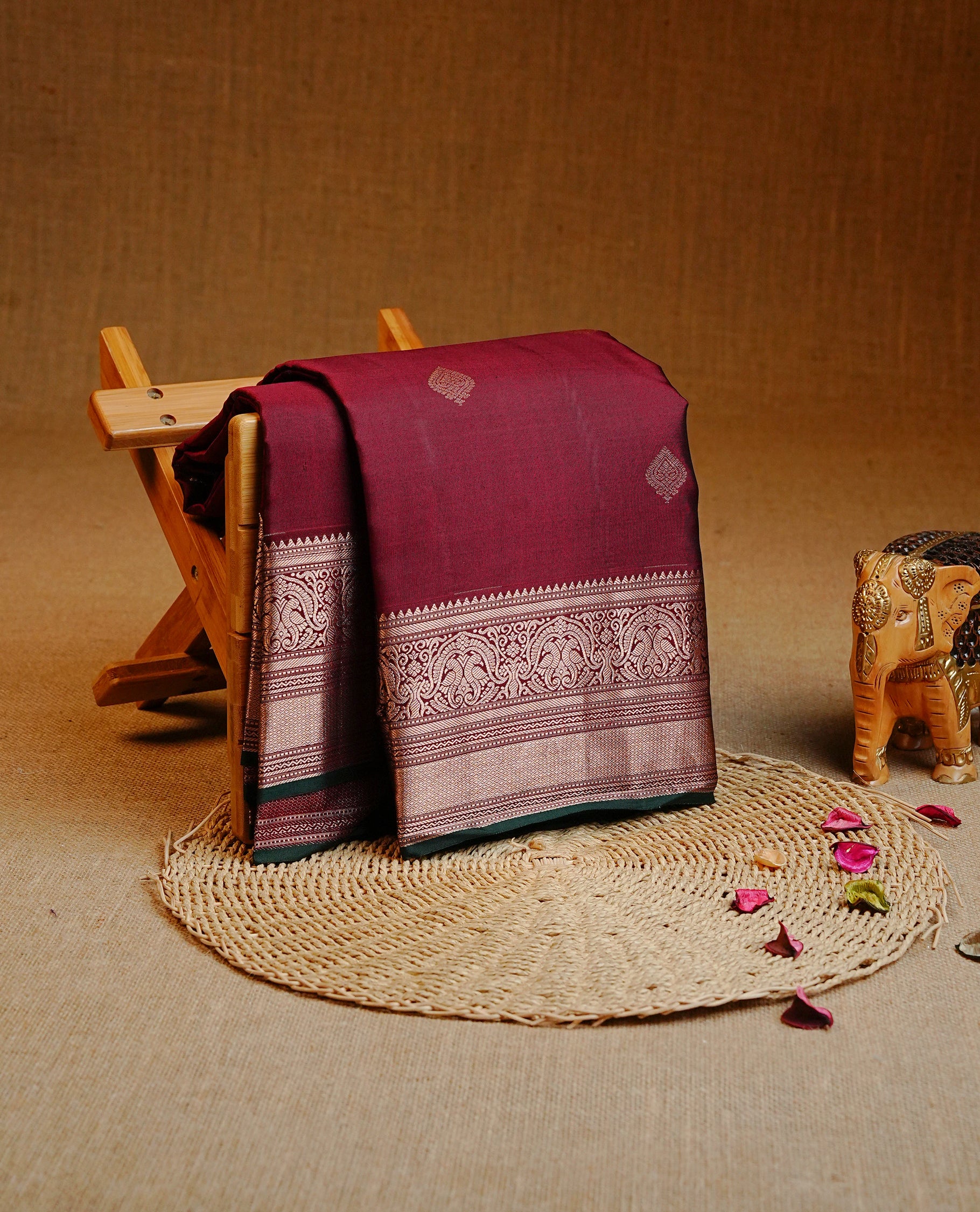 Maroon colour Kancheepuram Silk saree featuring Gold zari motifs on body, Enlighting Self Colour with Gold zari traditional & Green colour piping border, paired with a matching blouse piece.