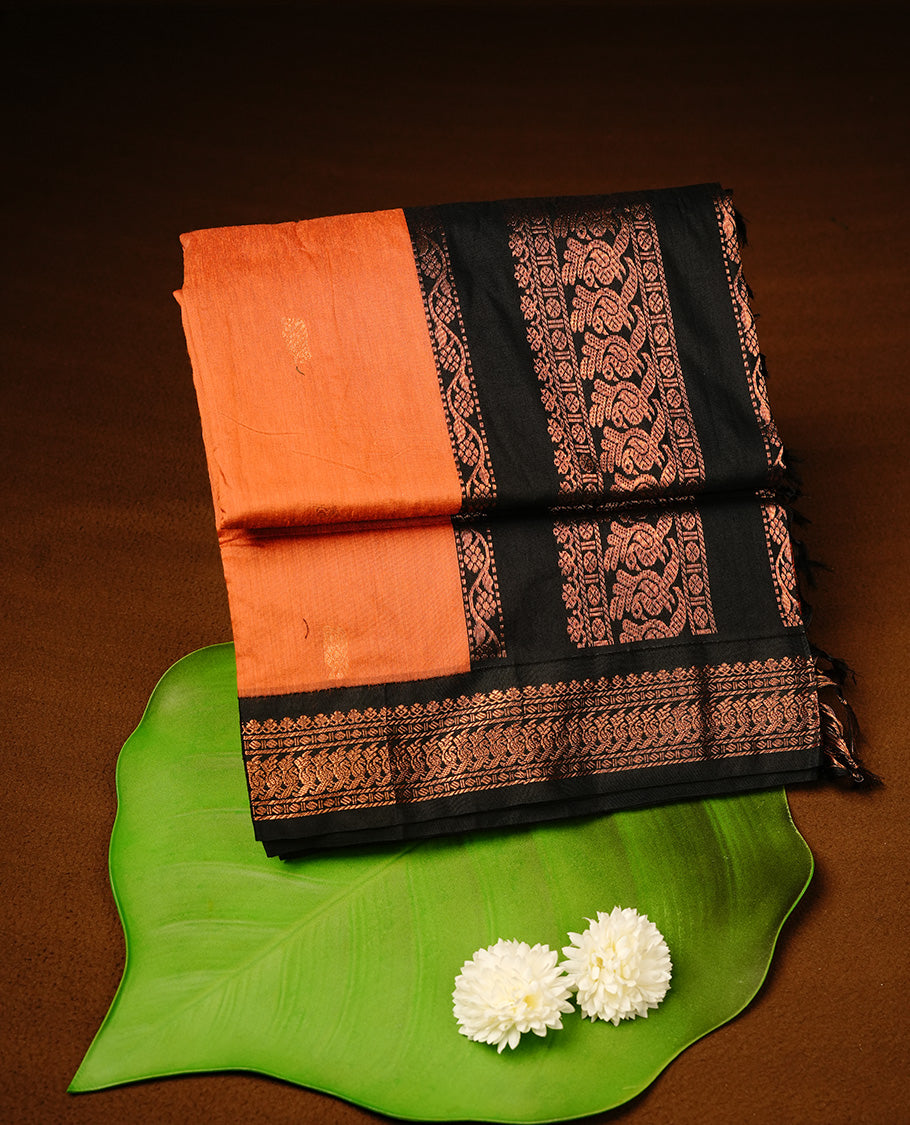 Orange colour kalyani cotton saree featuring gold zari motifs on body, highlighting contrast Black colour with Antique gold zari border, paired with matching blouse piece.