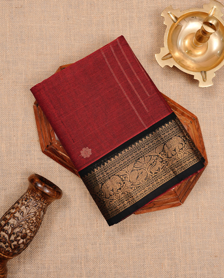 Dark red colour chettinad cotton saree featuring gold zari motifs on body, complemented by black colour with zari border, paired with matching blouse piece.