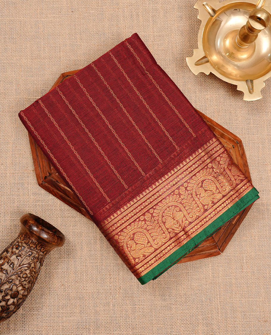 Maroon colour chettinad cotton saree featuring gold zari stripes on body, complemented by self colour with zari green colour piping border, paired with matching blouse piece.