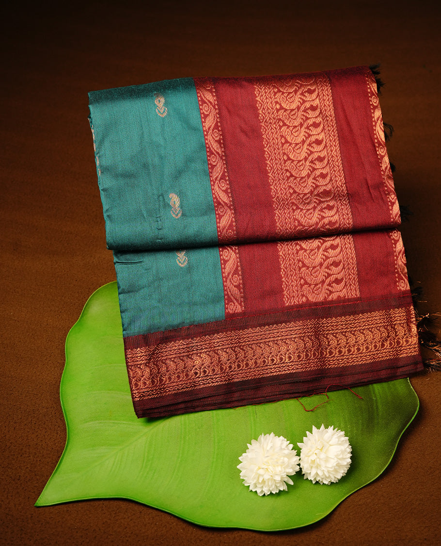 Teal green colour kalyani cotton saree featuring gold zari motifs on body, highlighting contrast Maroon colour with Antique gold zari border, paired with matching blouse piece.