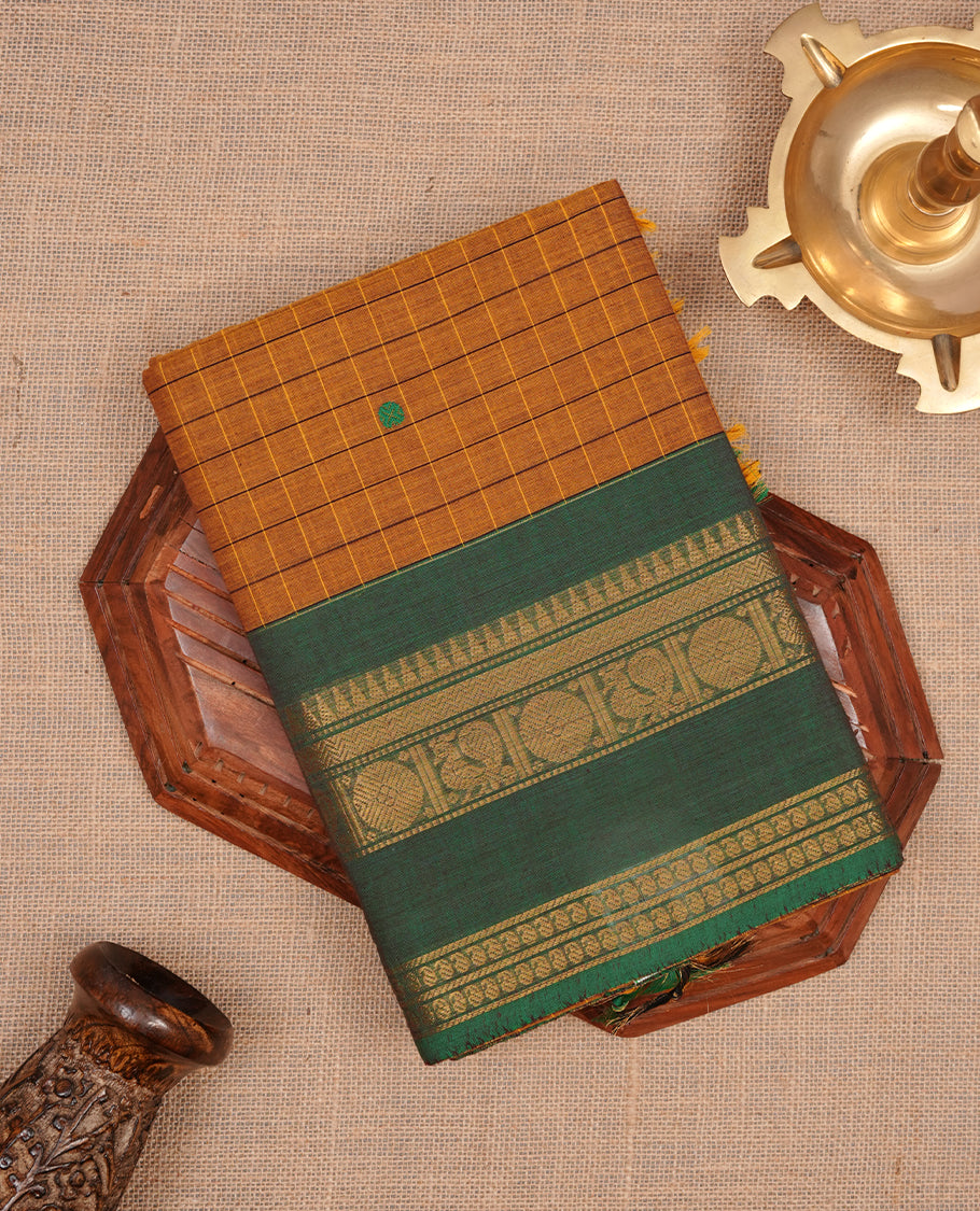 Mustard colour chettinad cotton featuring check pattern on body, complemented by contrast chocolate brown colour with gold zari border, paired with matching blouse piece.
