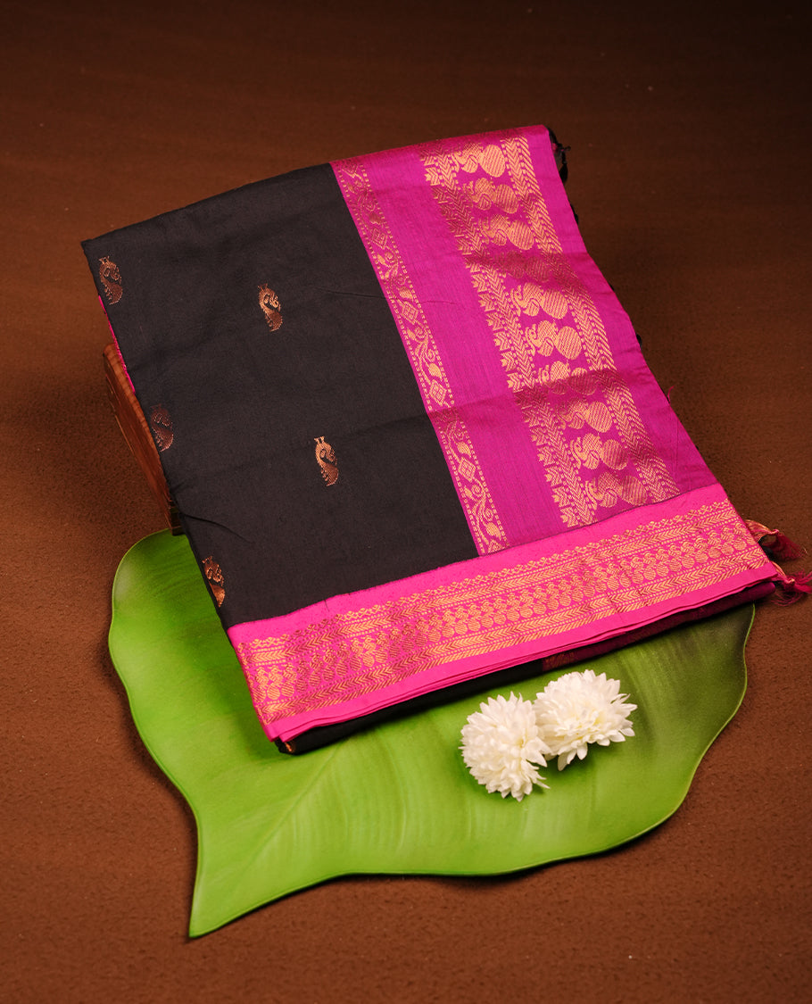 Black colour Kalyani cotton saree featuring delicate zari buttas on the body, complemented by a magenta zari border and woven pallu, paired with a matching blouse.