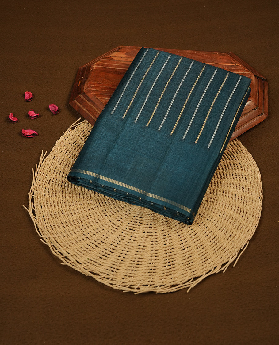 Teal colour semi tussar silk saree highlights gold and silver zari stripes across body, border, pallu and paired with matching blouse piece.