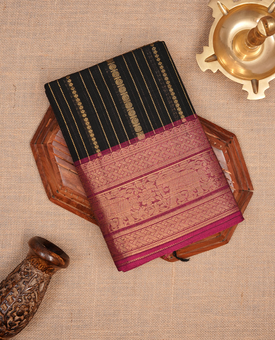 Black colour chettinad saree featuring gold zari stripes on body, complemented by contrast magenta colour with traditional border, paired with matching blouse piece.
