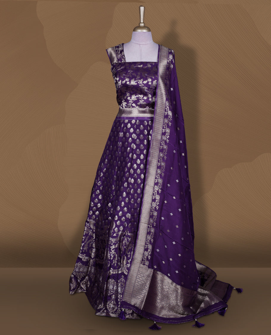 Purple colour Banarasi lehenga set with a stitched flared lehenga featuring all‑over zari butti motifs and rich woven border, paired with an unstitched floral zari blouse piece and matching dupatta with zari border and tasselled edges.