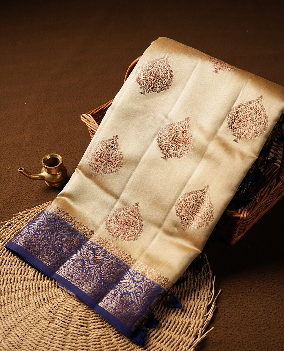 Cream beige Banaras soft silk saree with gold zari oval motifs on body, with contrast Blue colour floral pattern on pallu, border, and Matching blouse.