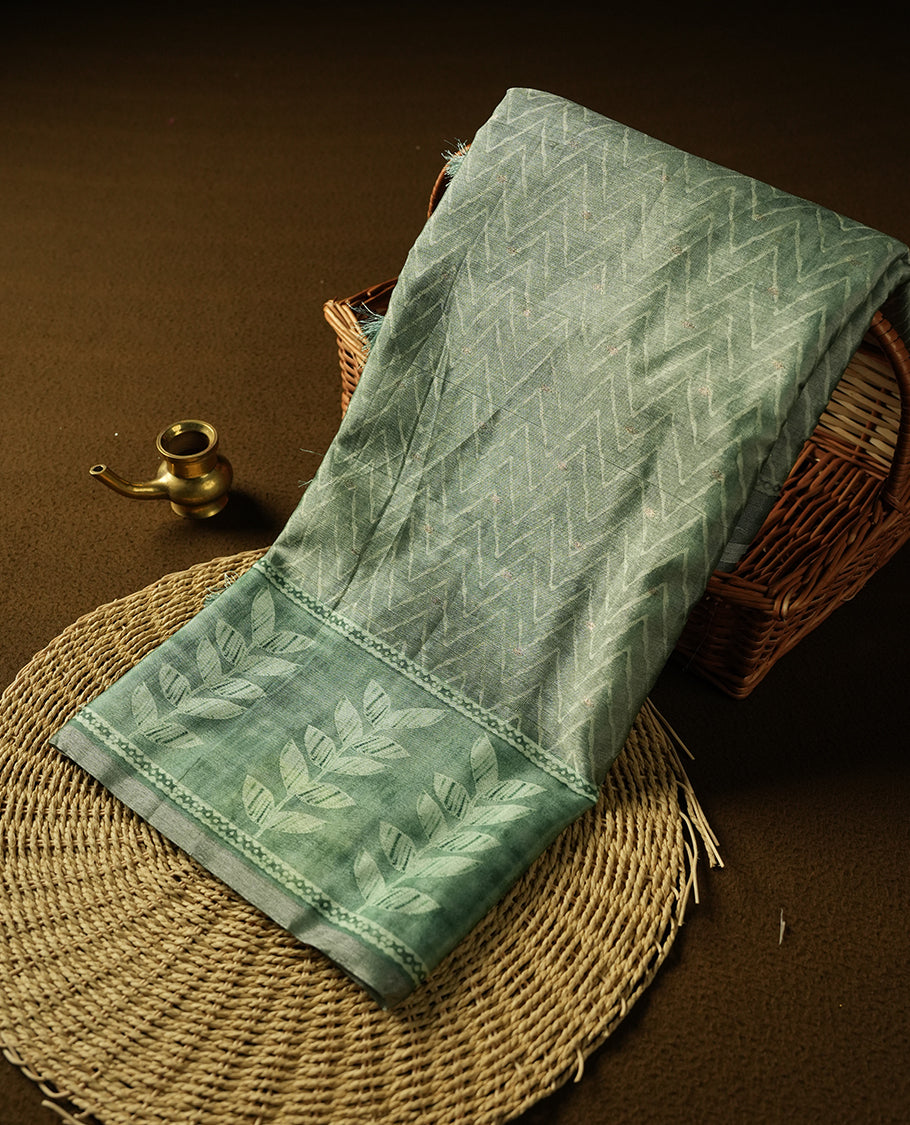 Sage green colour semi tussar saree adorned with Cream Zigzag printed pattern across the body and Leaf pattern on contrast Fern green colour border, paired with a matching blouse.