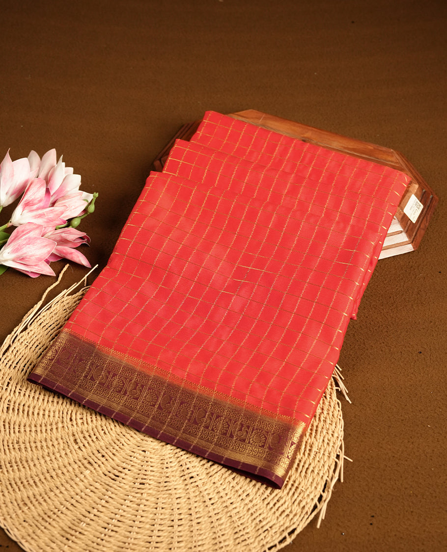 Red colour mysore crepe saree with gold zari check pattern on body, complemented by contrast Brown colour border featuring peacock and chakkram motifs, paired with matching blouse.