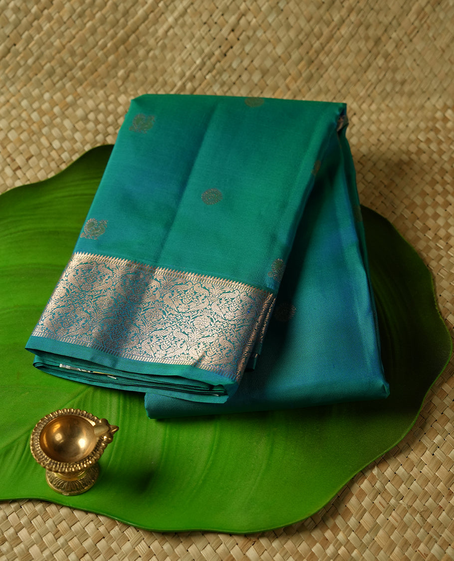 Peacock green colour Vasundhara silk saree adorned with all-over gold chakkaram& mayil motifs on the body, complemented by a self colour with rose gold traditional border and paired with a matching blouse piece.