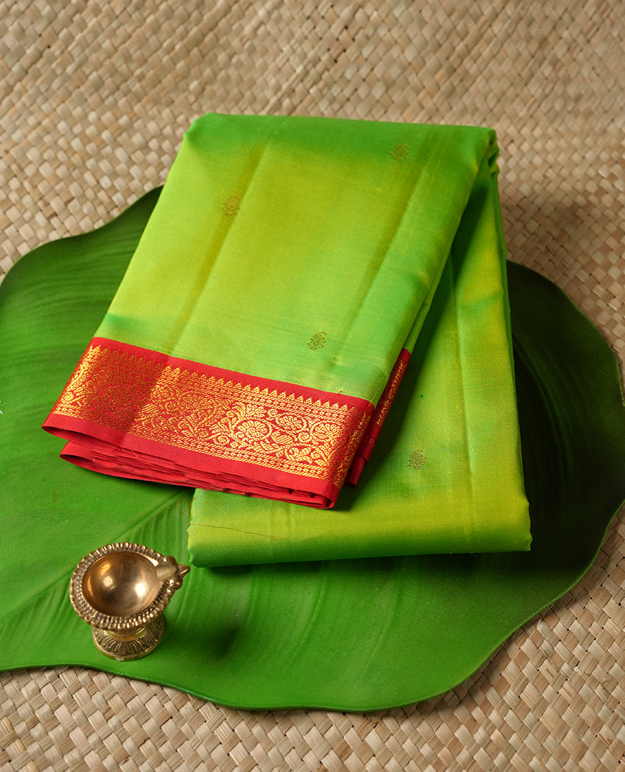 Lemon green colour Vasundhara silk saree adorned with all-over gold motifs on the body, complemented by a contrast red colour with gold simple traditional border and paired with a matching blouse piece.