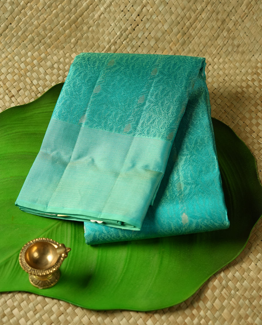 Aqua Green colour Vasundhara silk saree adorned with all-over green flower kodi motifs on the body, complemented by a self colour with gold Line pattern border and paired with a matching blouse piece.