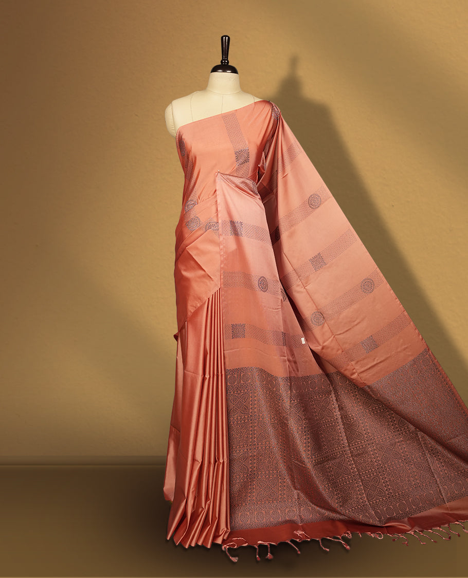 Amber rose colour semi soft silk saree, adorned with subtle self woven motifs on the body & The design is elevated with an elegant zari border & pallu with intricate detailing and tassel accents, paired with a matching blouse.