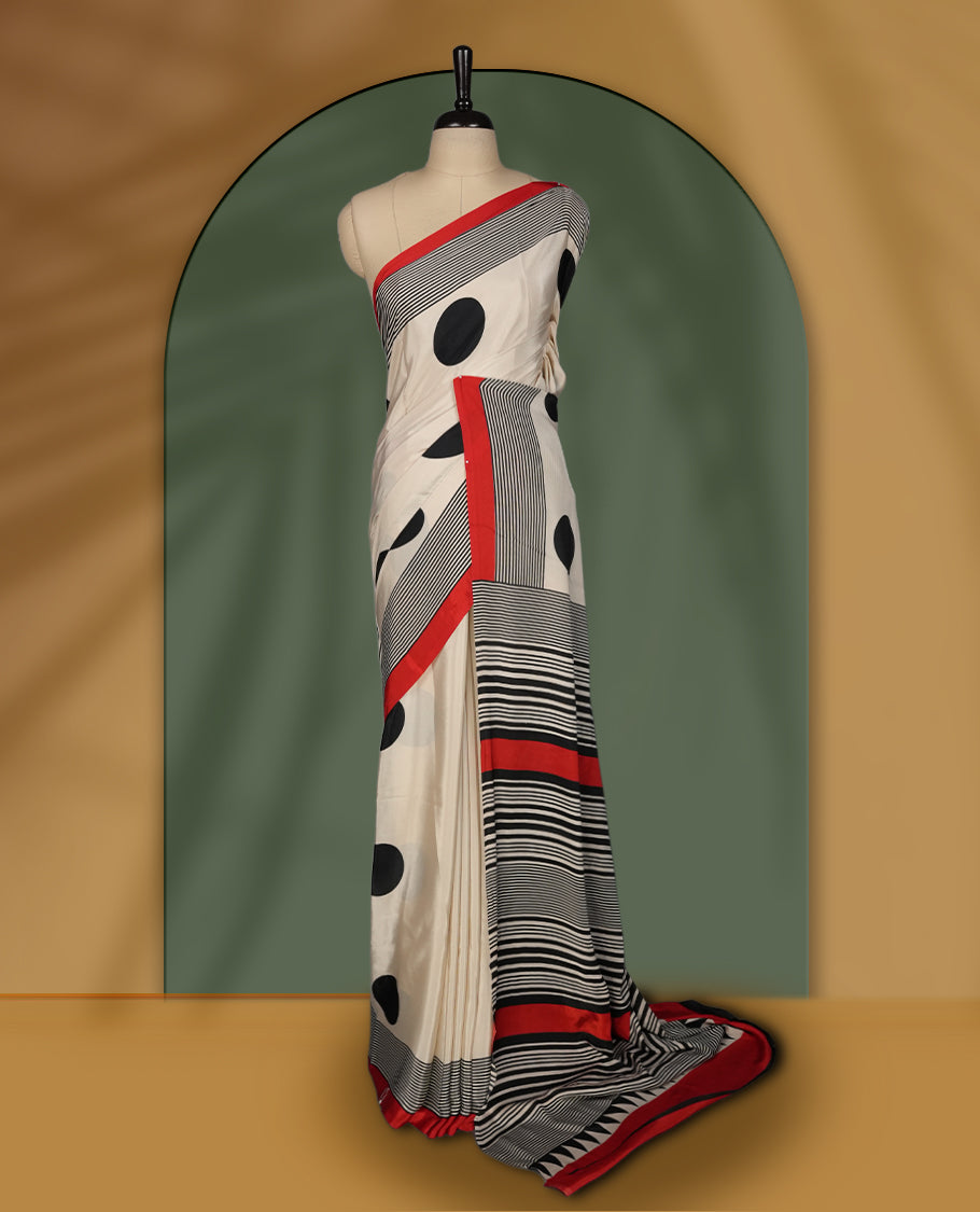 Cream colour saree with bold black polka dots, striped detailing, and striking red border & Comes with a stylish matching blouse.