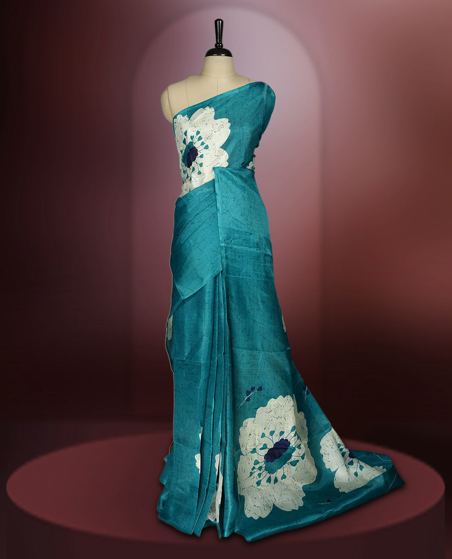 Teal blue colour saree with bold white floral motifs and subtle navy blue accents, exuding timeless elegance and modern charm, paired with a matching blouse.