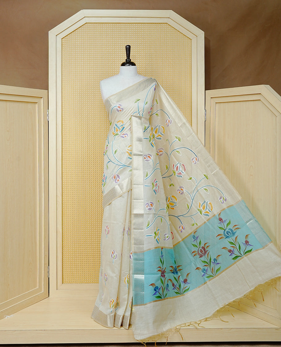 Cream Colour Tissue Kerala Saree Featuring Floral Kodi Threadwork Across The Body, Enhanced With A Light Gold Zari Border And A Light Blue Floral Pallu, Finished With Gold Tassels And A Matching Blouse Piece