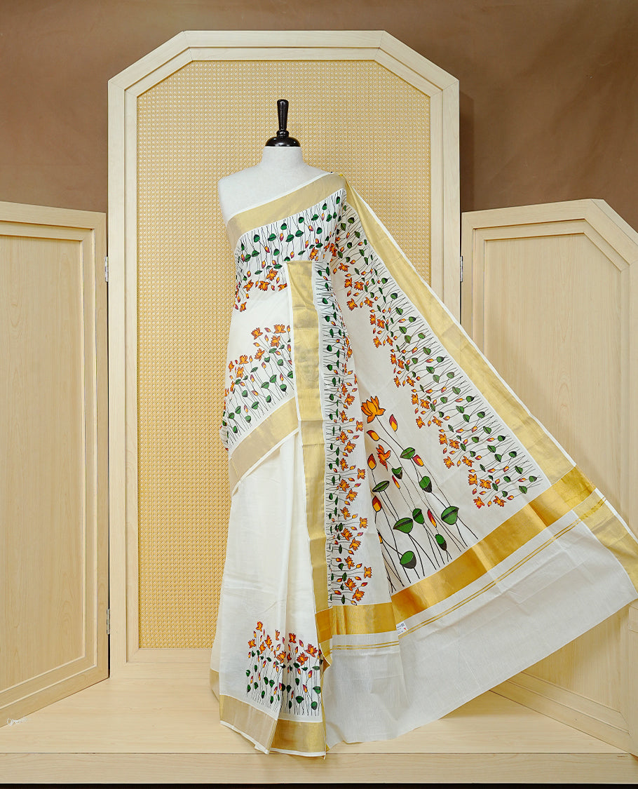 Cream Colour Cotton Kerala Saree Featuring Floral And Lotus Motifs On Body, With A Classic Gold Zari Border & A Gold Zari Pallu, Paired With A Matching Blouse Piece.
