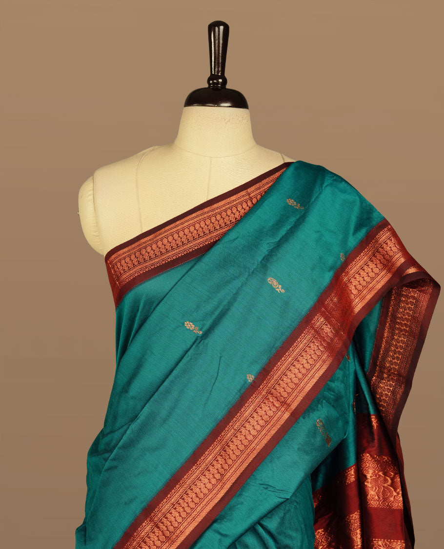 Teal colour kalyani cotton saree featuring antique zari motifs on body, complemented by Maroon colour with Antique zari border, paired with matching blouse piece.