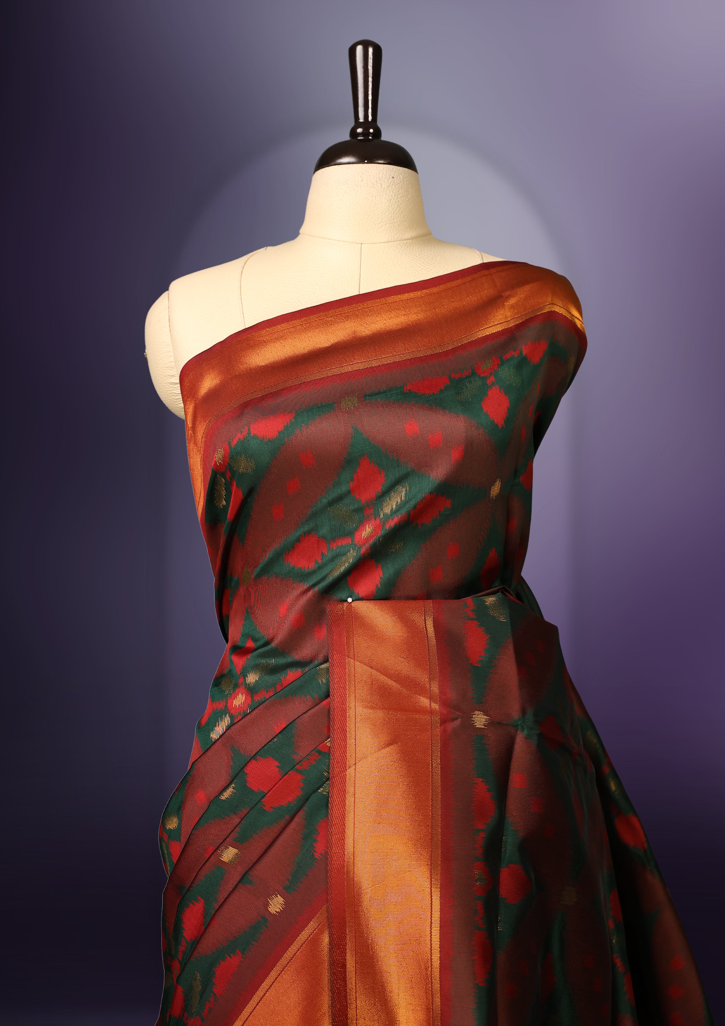 Maroon and green Ikat silk saree featuring intricate woven geometric and floral motifs across the body and pallu, complemented with a golden brown zari border and tassels, paired with a matching blouse piece.