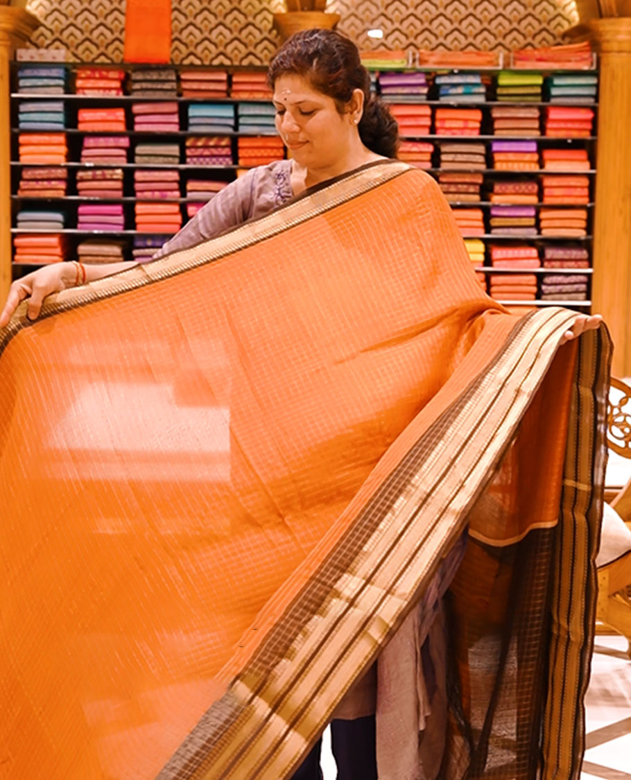 Rust orange colour moss chiffon saree featuring gold zari checks designed body, complemented by contrast Chocolate colour zari jacquard border, paired with contrast colour blouse piece.